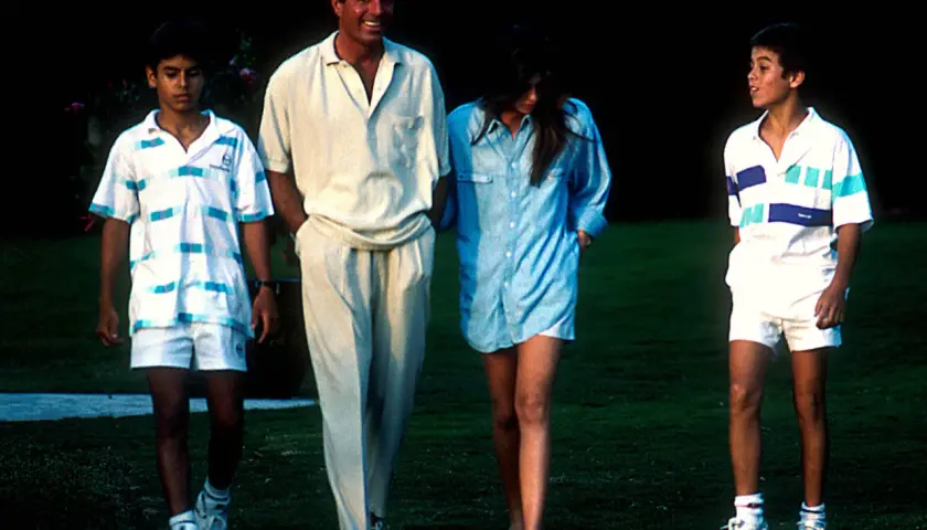 Julio Iglesias z dziećmi, dwoma synami i córką, spacerują po trawniku w letnich strojach.