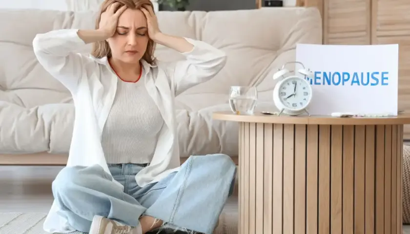 Kobieta z bólem głowy podczas menopauzy, obok tabletki i budzik.