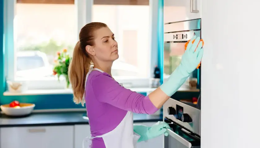 Kobieta w fartuchu i rękawiczkach czyści piekarnik. Soda oczyszczona na co pomaga? W kuchni, do czyszczenia!