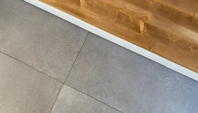 Le piastrelle grigie con venature sottili si incontrano sotto un piano in legno scuro, creando un contrasto moderno.
