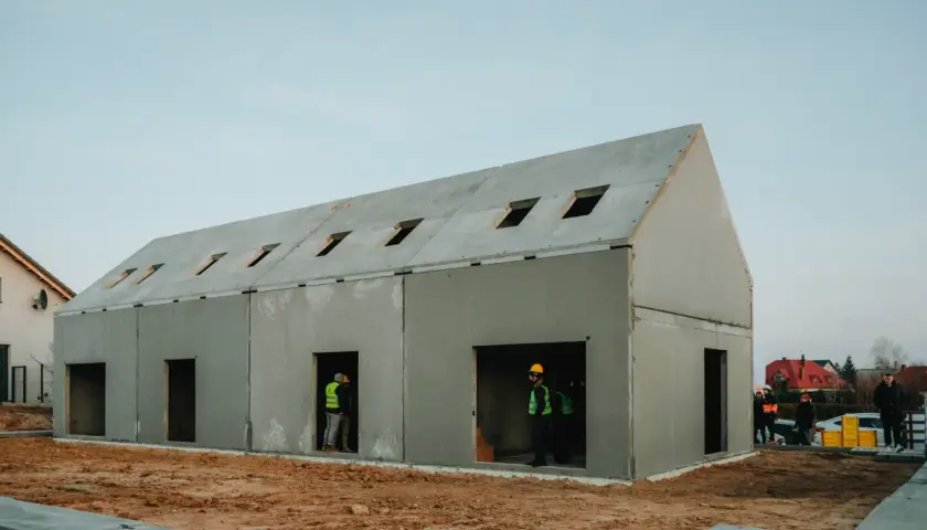 Budowa domu z gotowych elementów betonowych. Widać pracowników w kamizelkach odblaskowych.