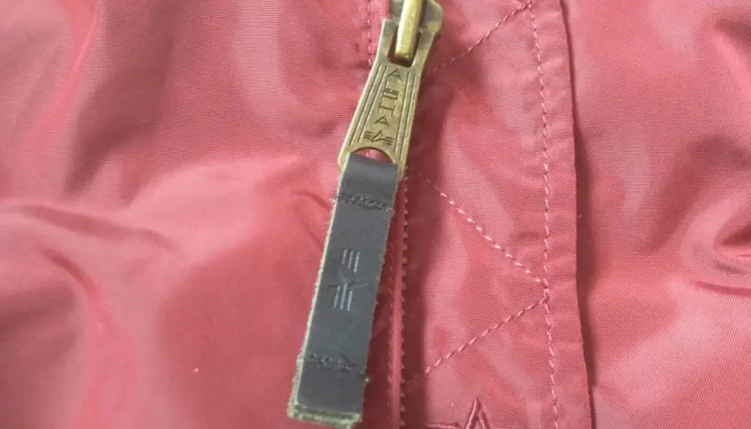 Zamek kurtki Alpha Industries z logo. Detale materiału i szwów, pomocne przy wyborze alpha industries rozmiarówka.