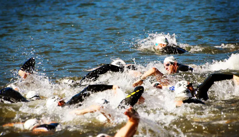 Zawodnicy walczą o pozycję podczas pływania na dystansie 1/2 ironman. Woda wzburzona, widać kaski i okulary.
