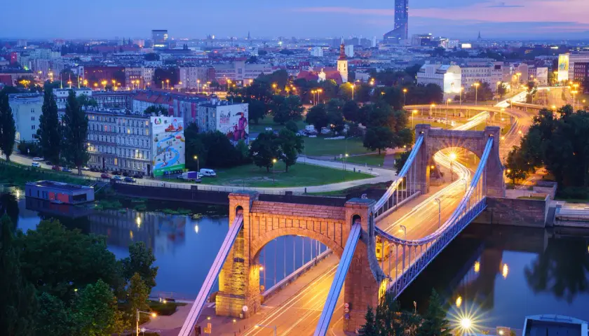 Most Wrocławia w niebieskiej godzinie w fotografii. Most Grunwaldzki i miejska panorama nocą, z rozmazanymi światłami samochodów tworzącymi smugi.
