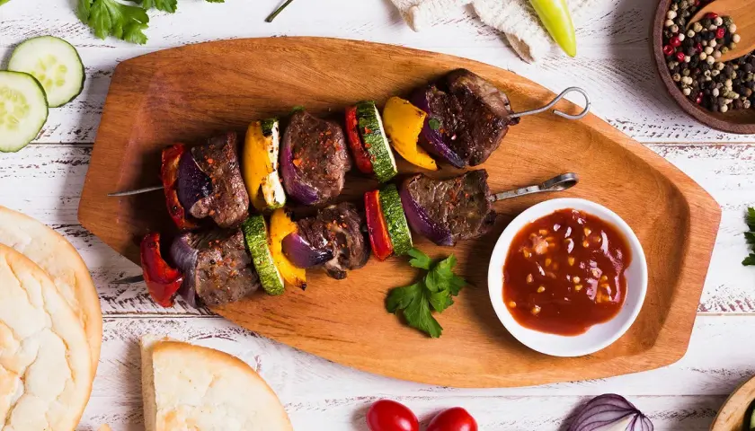 Brochette de rumsteck grillée avec poivrons, courgettes et oignons, servie avec une sauce savoureuse.