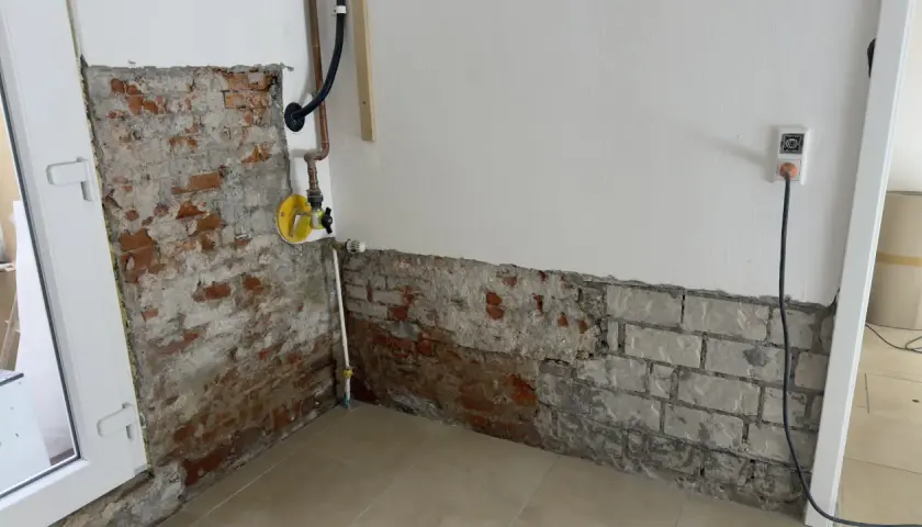 Baustelle mit freiliegendem Mauerwerk und Rohren. Ein gelbes Ventil deutet auf eine bevorstehende Maßnahme wie das Injektionsverfahren Horizontalsperre hin.