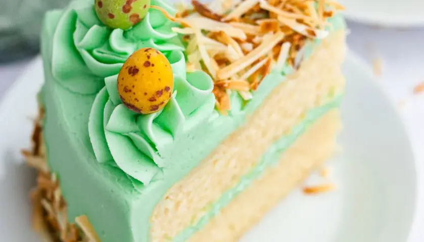 Rebanada de pastel verde menta con glaseado, decorada con huevos de pascua y coco tostado. ¡Ideas de pasteles de Pascua!