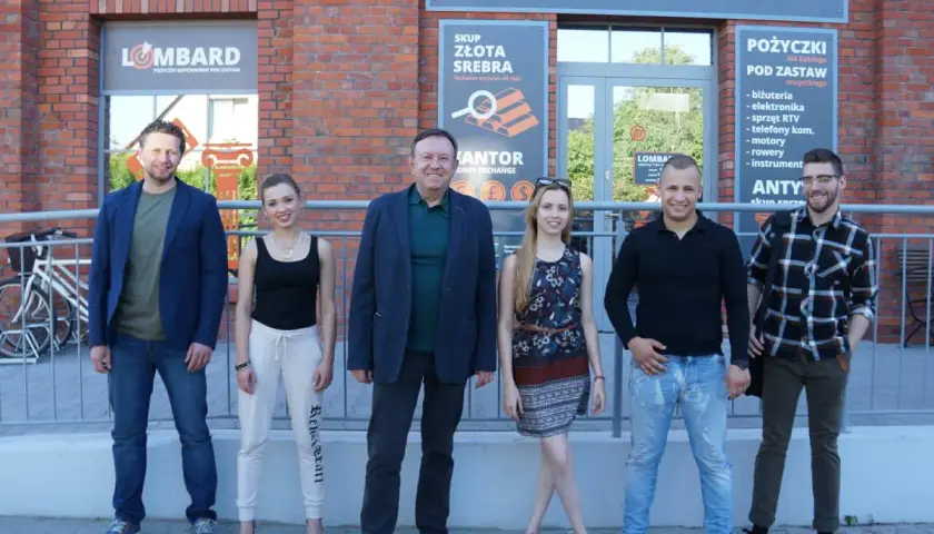 Lombard życie pod zastaw obsada: uśmiechnięci pracownicy lombardu pozują przed budynkiem.