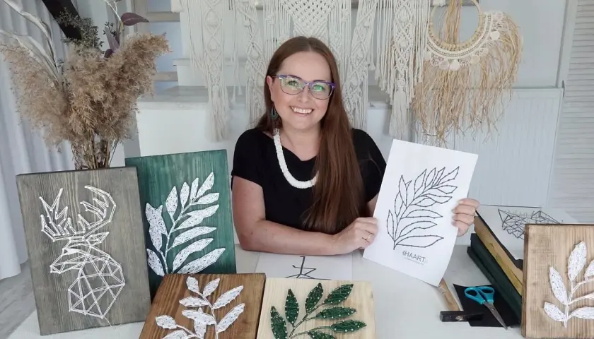 Kobieta prezentuje swoje prace string art, w tym jelenia i liście. Pokazuje też szablony do string art, które pomagają tworzyć piękne dekoracje.