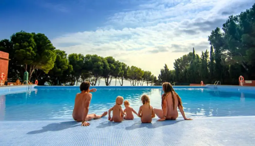 Famille profitant d'une journée ensoleillée au bord de la piscine dans un camping naturiste au Portugal.