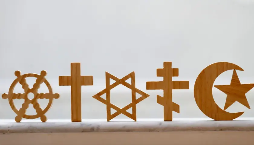 Drewniane symbole religijne: koło Dharmy, krzyże, Gwiazda Dawida, półksiężyc z gwiazdą. Pokazują różnorodność wierzeń, jak w Bangladeszu religia.