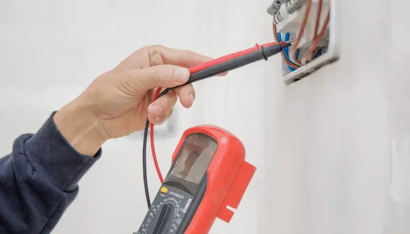 Elektryk sprawdza instalację elektryczną multimetrem, przygotowując protokół odbioru.