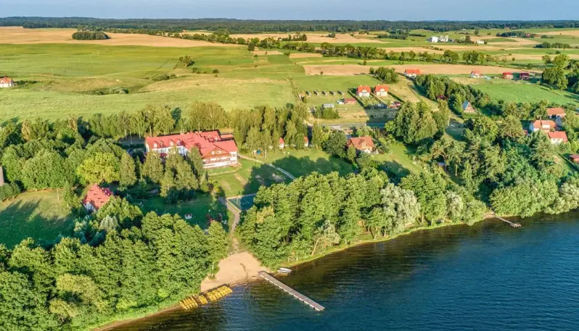 Widok z lotu ptaka na domki letniskowe nad jeziorem w Mikołajkach, z pomostem i żółtymi kajakami.