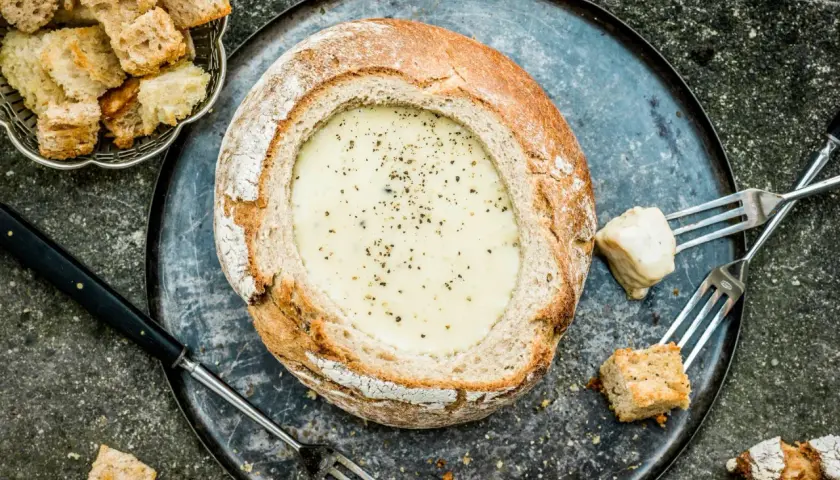 Une généreuse quantité de pain est prête à être trempée dans cette fondue savoyarde crémeuse, servie dans un pain rond.