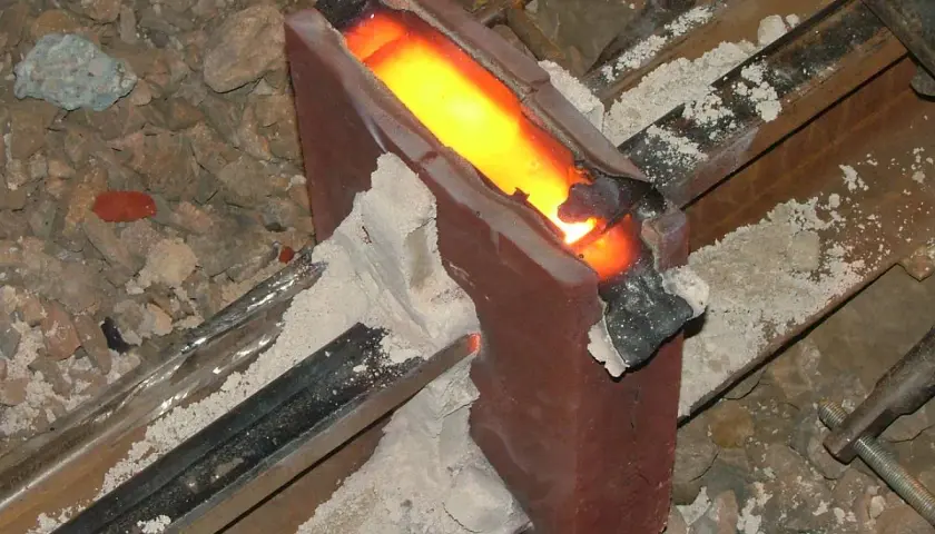 Żelazny szynoprzewód połączony metodą spawania termitowego. Roztopiony metal płynie w formie, tworząc mocne połączenie.