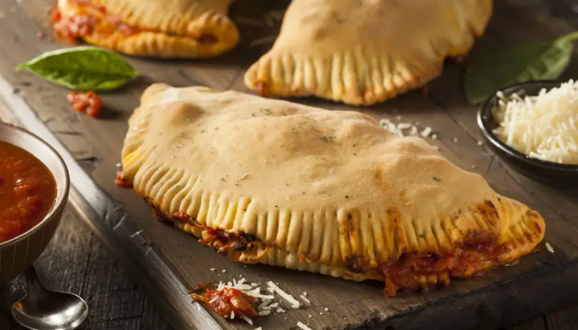 Pyszny calzone z kurczakiem, sos pomidorowy, starty ser i świeża bazylia na drewnianej desce.