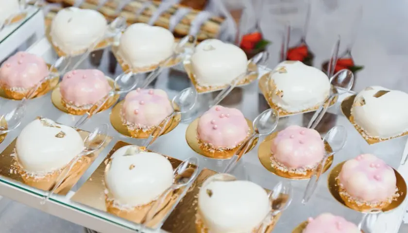 Eleganckie finger food w kieliszkach: serduszka i kwiatki w białej i różowej polewie, ozdobione perełkami i płatkami złota.