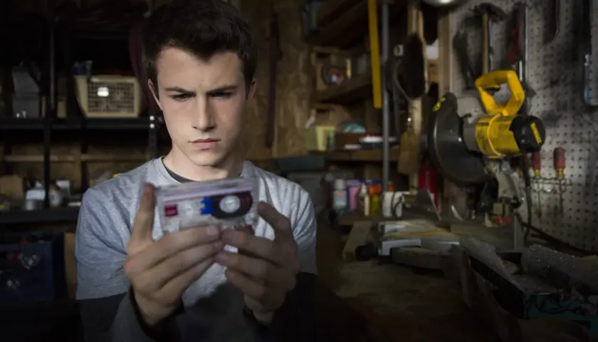 Clay Jensen z serialu "13 powodów" trzyma kasetę z nagraniem w warsztacie pełnym narzędzi.