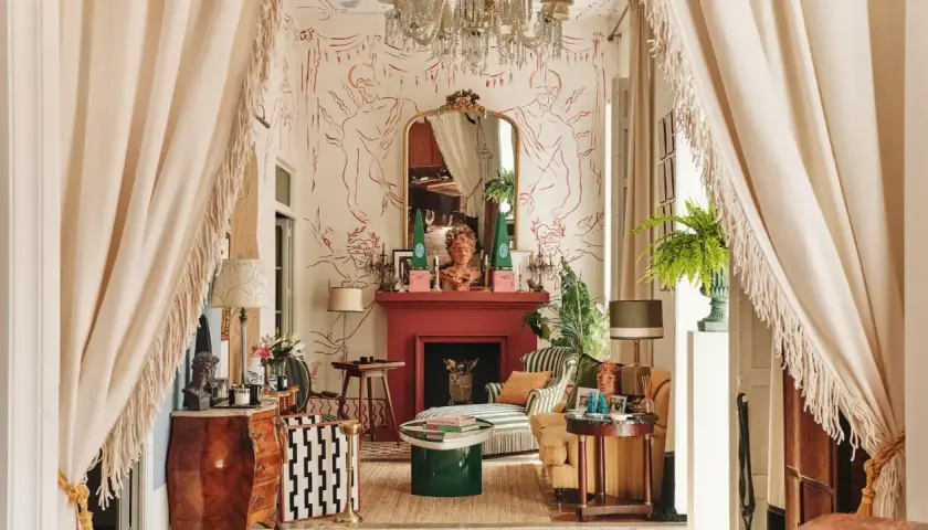 Salon éclectique avec papier peint aux figures rouges, cheminée rouge, mobilier ancien et moderne, rideaux à franges.