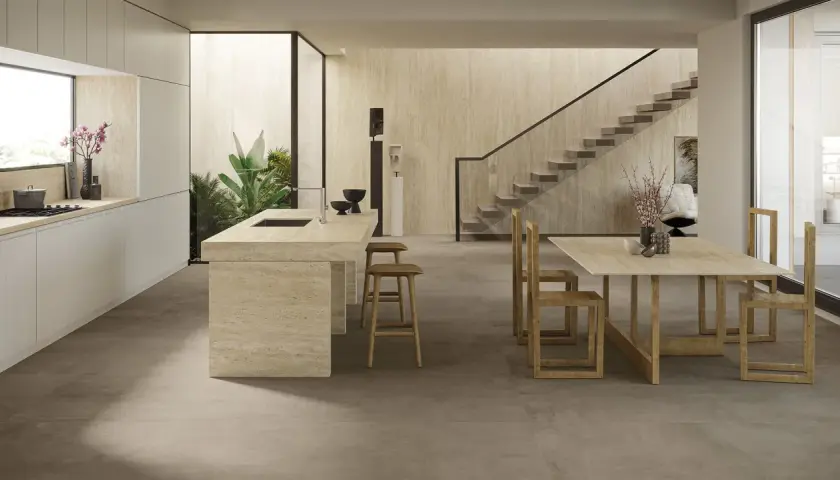 Cucina moderna con isola in travertino e tavolo in legno. Il pavimento non rettificato crea un effetto materico e continuo, integrandosi con le pareti in pietra.