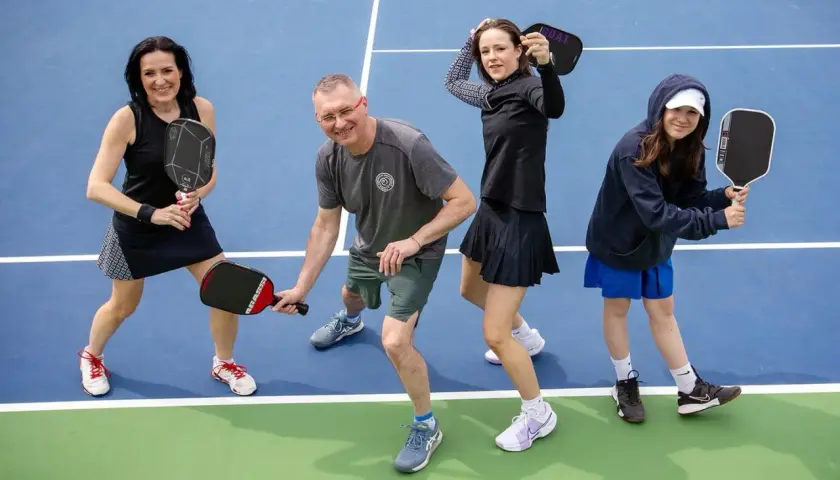 Rodzina na korcie do pickleball, co to za sport? Wszyscy trzymają rakietki, gotowi do gry.