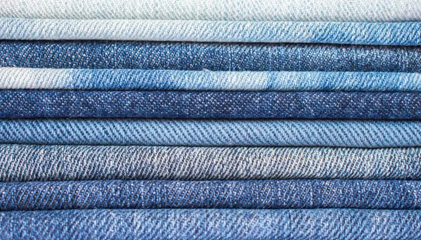 Pile de jeans bleus de différentes teintes. Le jean est fait de coton, un tissu résistant et confortable.