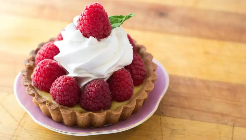 Tartelette garnie de framboises fraîches et d'une délicate crème chantilly, évoquant l'origine d'une douceur intemporelle.