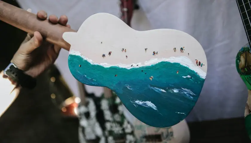 Un ukulélé peint d'une scène de plage animée. La taille ukulele est parfaite pour emporter cette œuvre d'art en voyage.