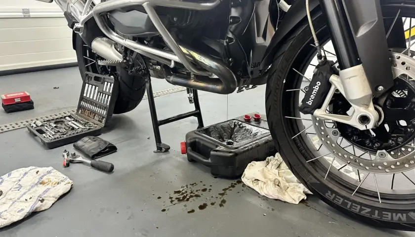 Motocykl na stojaku, narzędzia i pojemnik na zużyty olej.