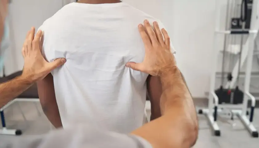 Fizjoterapeuta bada plecy pacjenta, szukając przyczyny bólu kręgosłupa piersiowego.