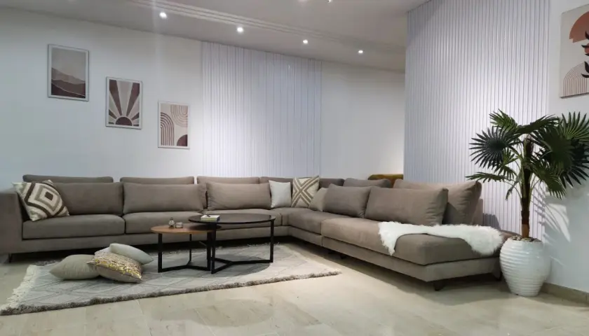 Un grand canapé d'angle taupe, parfait pour réfléchir à quelle couleur de canapé choisir. Décoration murale et plante verte complètent l'ensemble.