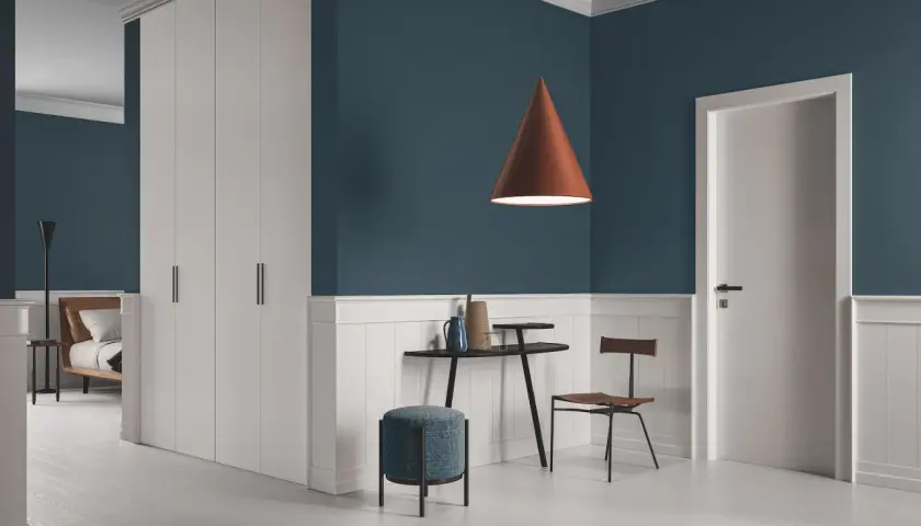 Un soggiorno moderno con pareti blu intenso e battiscopa bianco. Un lampadario color terra e infissi marroni creano un contrasto caldo.