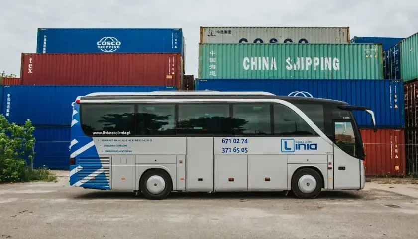 Biały autobus z napisem "Linia Nauka Jazdy" stoi na tle kontenerów. Chcesz wiedzieć, jakie prawo jazdy na busa? Ta szkoła jazdy oferuje kursy na kategorie od AM do D1.