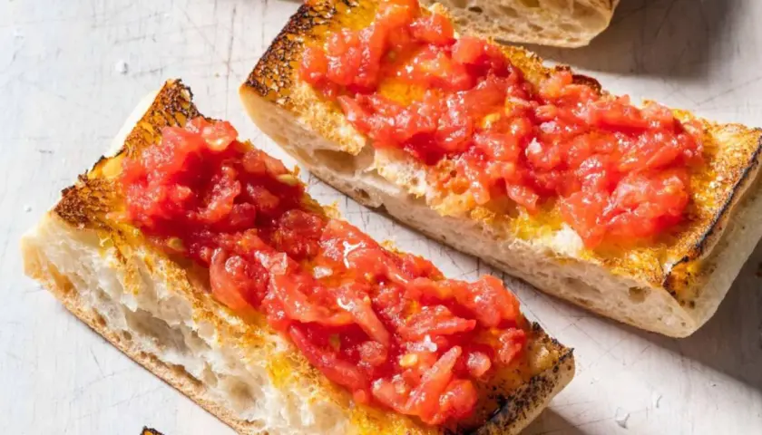 Rebanadas de pan tostado cubiertas con tomate rallado y aceite de oliva, un delicioso pan tumaca.