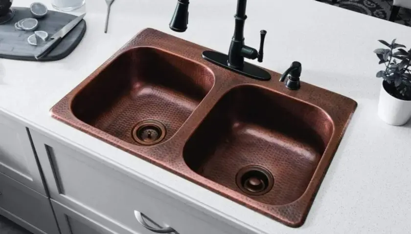 Fregadero doble de cobre martillado con grifo negro. Un truco para limpiar cobre con vinagre es ideal para mantenerlo brillante.