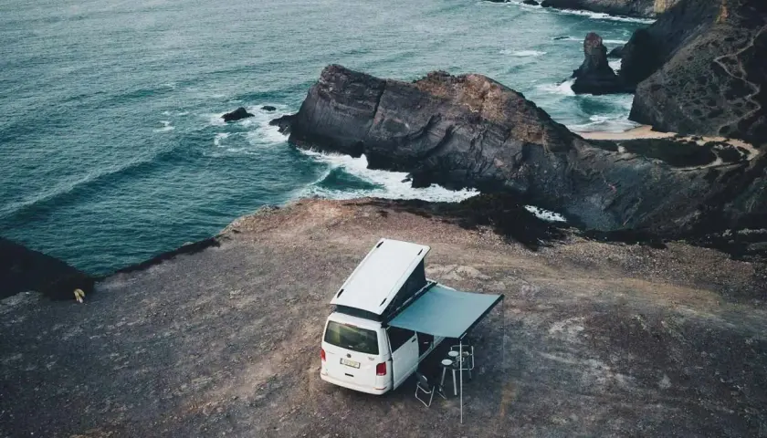 Furgoneta camper con toldo desplegado en un acantilado, disfrutando del camping en el norte de Portugal. El mar azul choca contra las rocas.