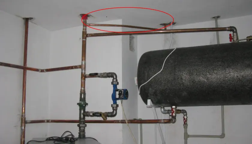Instalacja hydrauliczna z bojlerem i pompą obiegową. Pokazano fragment instalacji, jak podłączyć zawór bezpieczeństwa do bojlera, z widocznymi rurami miedzianymi i złączkami.