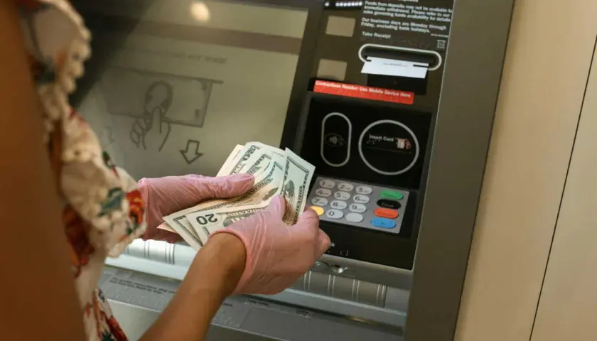 Une personne avec des gants roses prépare un dépôt d'argent liquide à un guichet automatique.
