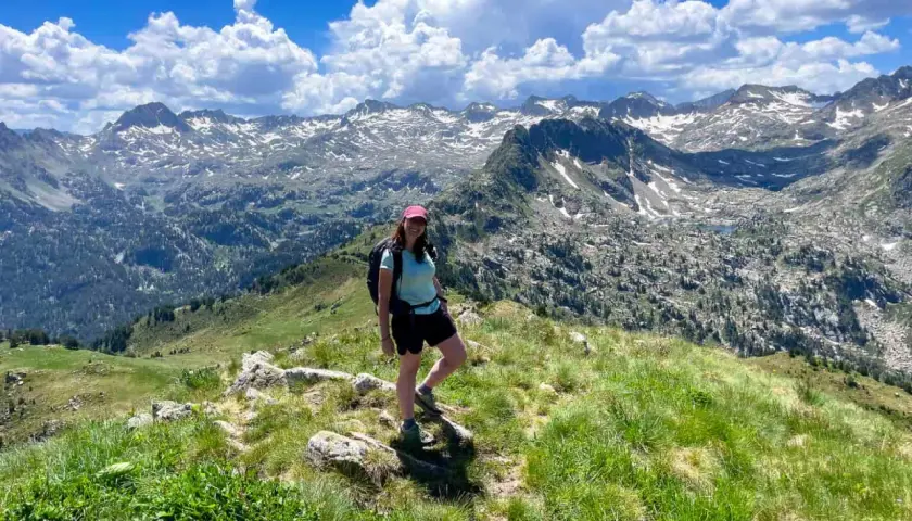 Senderista disfruta de las impresionantes vistas de las rutas del Valle de Arán, con picos nevados y un cielo azul con nubes.