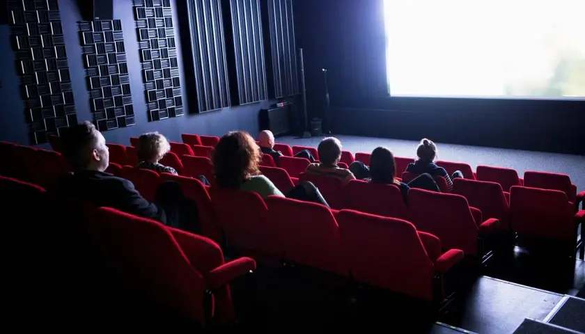 Publiken sitter i röda biosalongsstolar och tittar på en ljus bioduk. Klara biografen är redo för filmvisning.