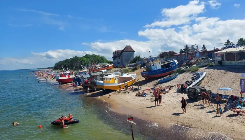 Słoneczne **morze bałtyckie wakacje** z kolorowymi łodziami na plaży i tłumem ludzi cieszących się słońcem.