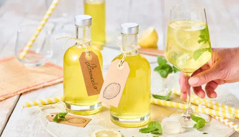 Zwei Flaschen mit gelbem Limoncello, ein Glas mit Eis, Zitrone und Minze. Das ist das original italienische Limoncello Rezept.