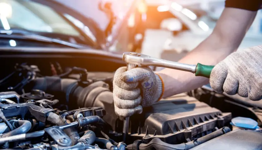 Mechanik w rękawicach dokręca śrubę kluczem nasadowym w silniku samochodu. Może to być naprawa po problemach po płukance silnika.