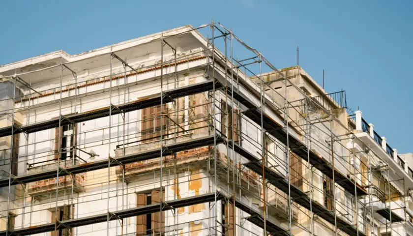 Bâtiment en rénovation, échafaudages pour aide ravalement façade sans isolation extérieur. Le ciel est bleu.