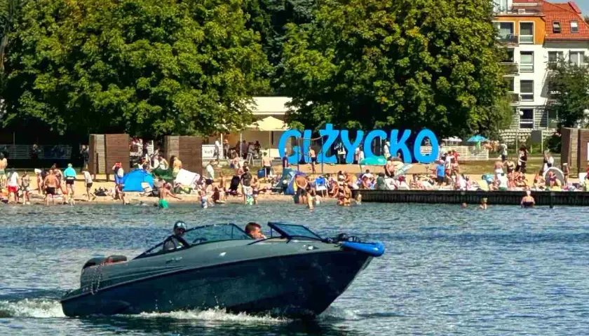 Motorówka sunie po wodzie, obok plaży w Giżycku. Idealne miejsce na odkrywanie mazurskich szlaków wodnych.