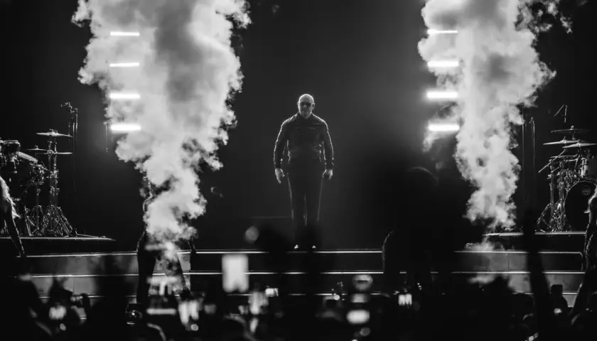 Pitbull na scenie, otoczony dymem i światłami, podczas koncertu.