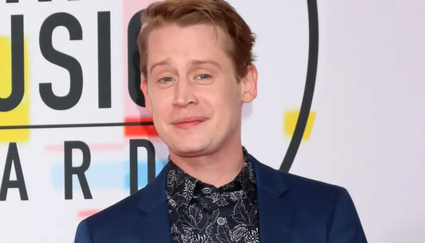 Macaulay Culkin, żyje i ma się dobrze, pozuje na tle napisu "MUSIC AWARDS".