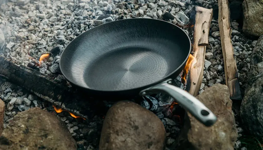 Poêle posée sur des braises et des pierres, prête à redresser le fond d'une poêle pour une cuisson en plein air.