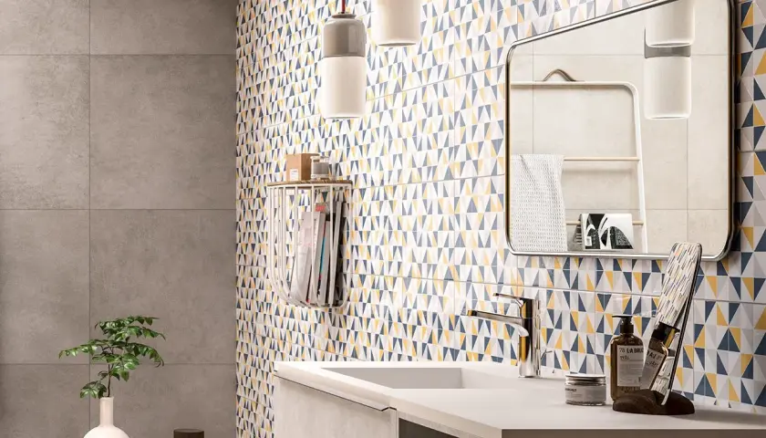Un bagno moderno con piastrelle geometriche colorate che coprono le pareti. Un lavandino minimalista e un grande specchio completano l'arredo.