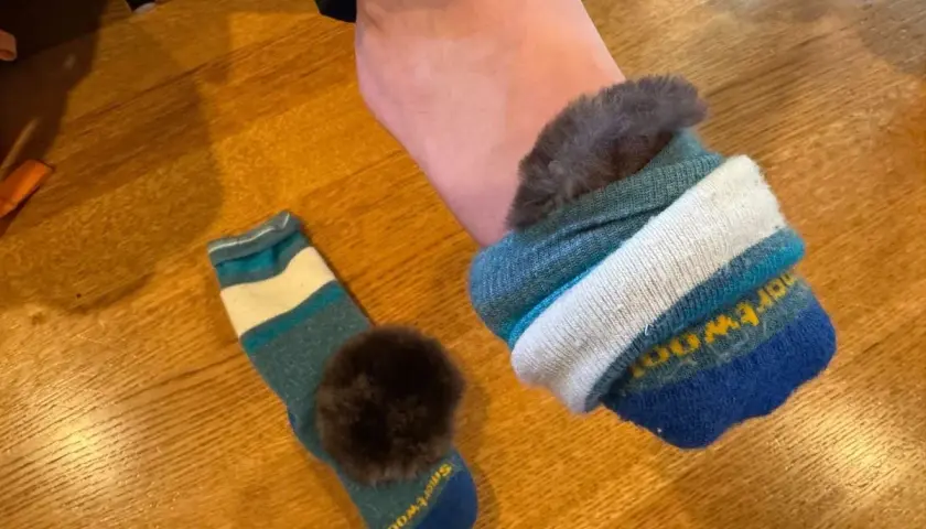 A foot wearing a fluffy-lined sock, with another striped sock and pom-pom nearby. Perfect for learning how to keep feet warm in boots.